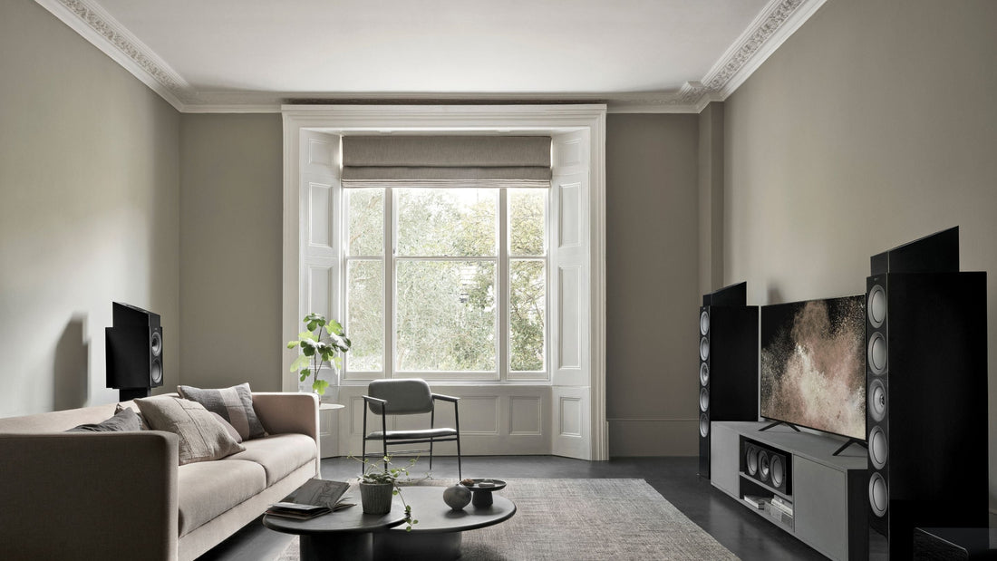 Modern living room with grey sofa, coffee table, and wall-mounted television, surrounded by R Series HiFi Meta speakers
