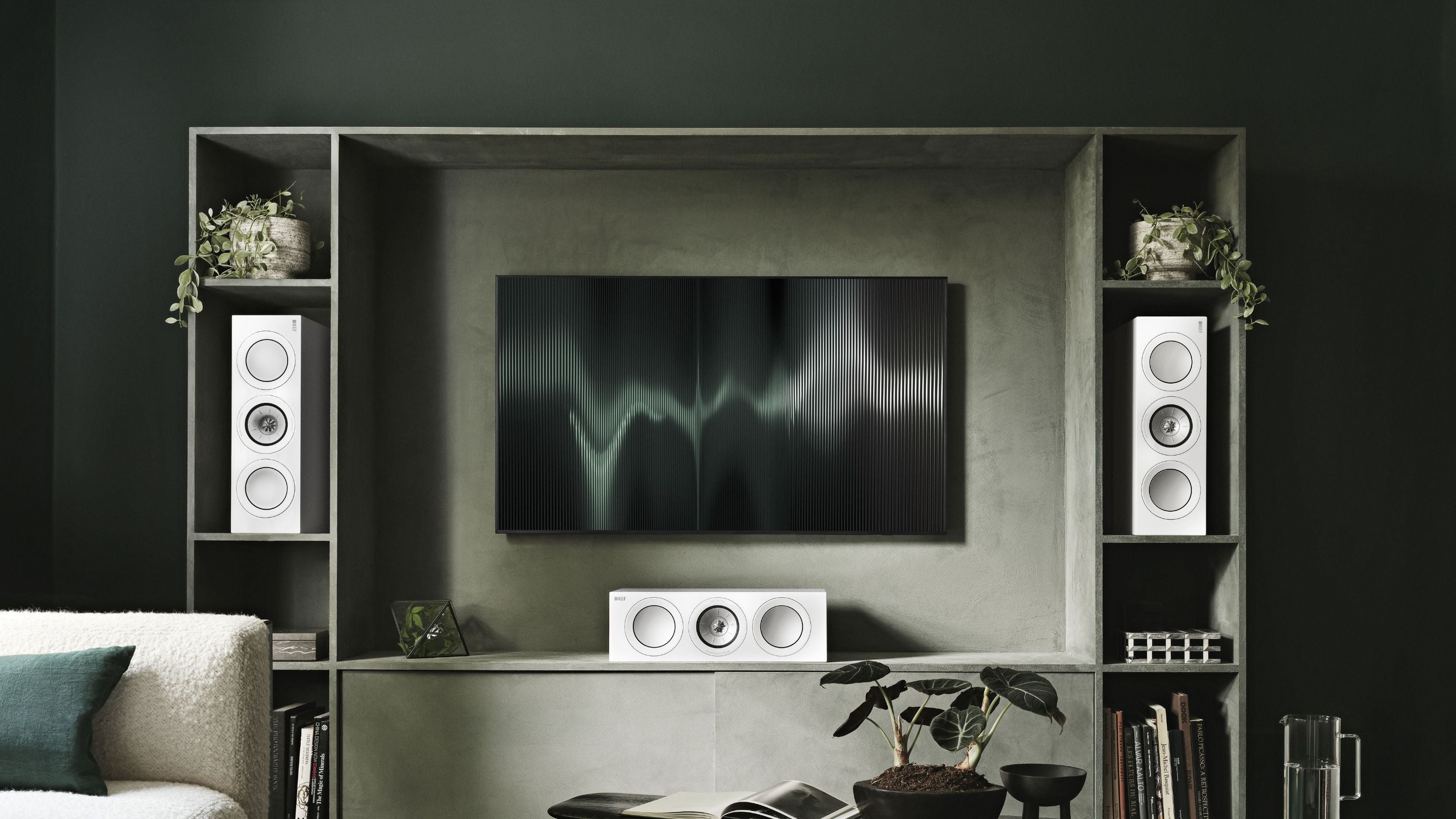 A modern living room showcasing a wall-mounted television with a Pair of R6 Meta centre channel speakers above a stylish couch, designed for relaxation and entertainment.