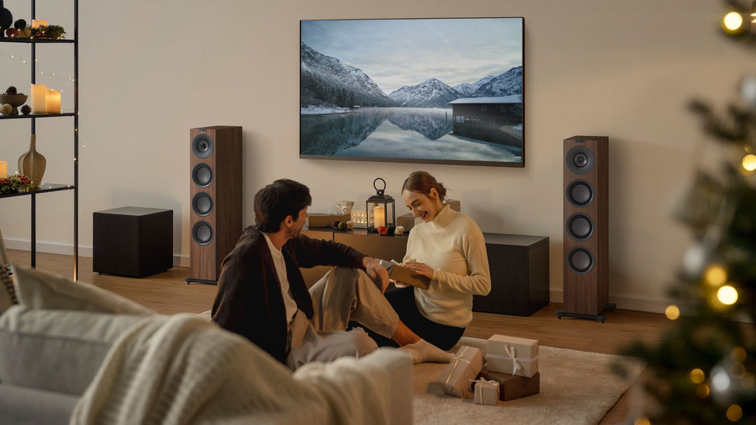 Living room with a couple sitting on a couch, surrounded by decorative items and a large TV screen.