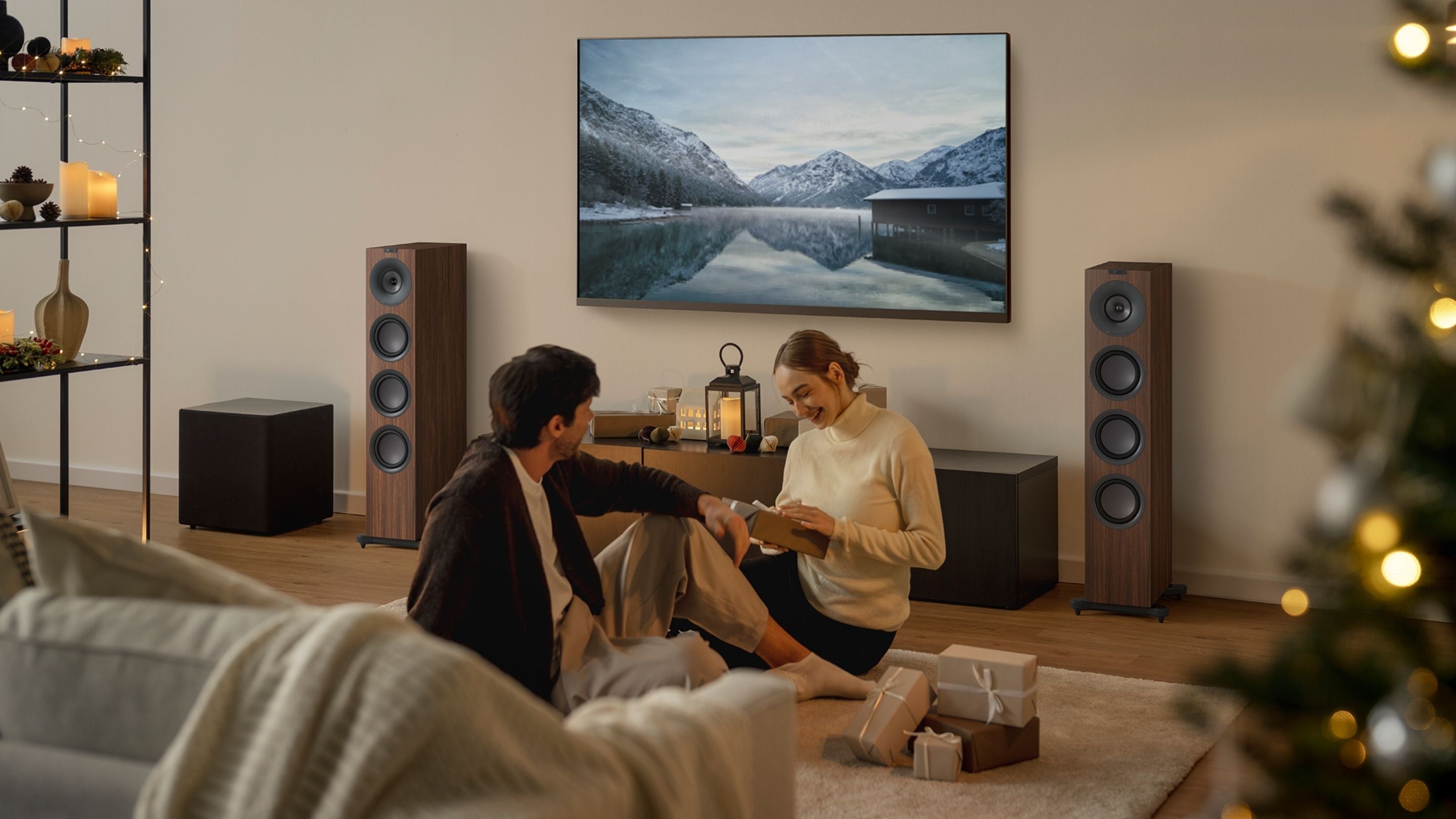 Living room with a couple sitting on a couch, surrounded by decorative items and a large TV screen.