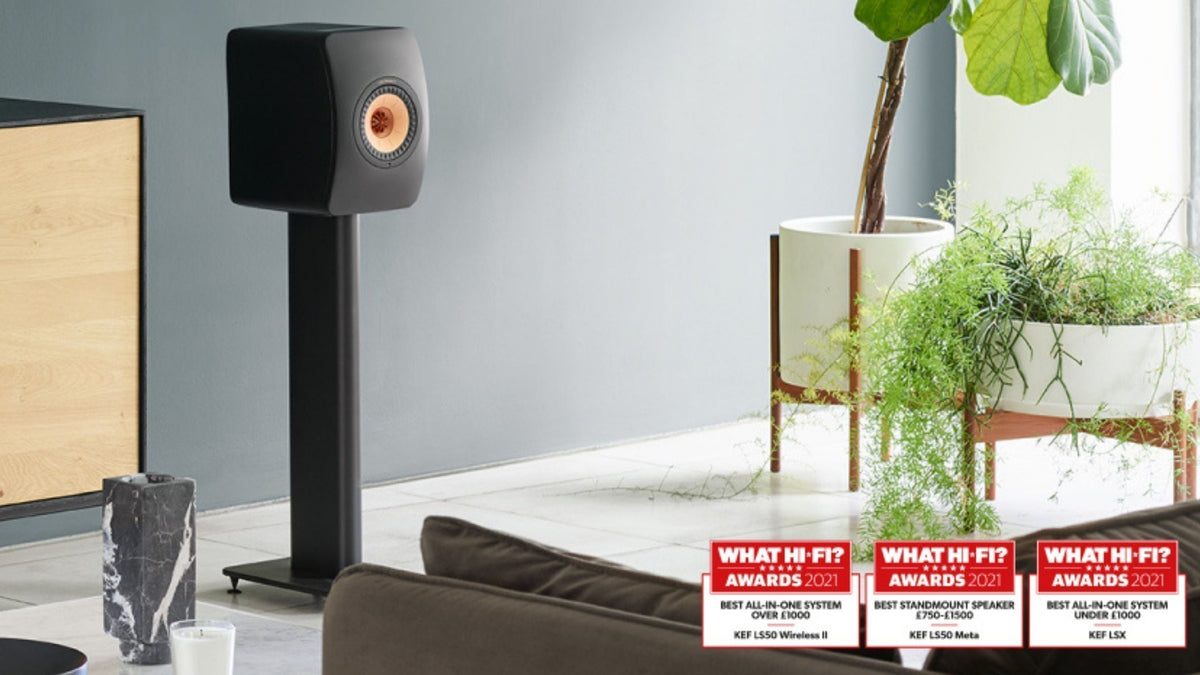 LS50 Wireless II Black speaker on a stand in a modern living room with plants and awards displayed.
