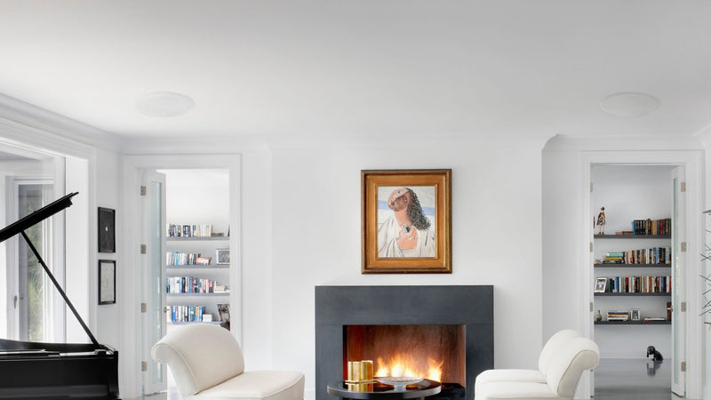 KEF architectural speakers ci250rrb-thx installed in the ceiling of a living room featuring a piano and a fireplace.